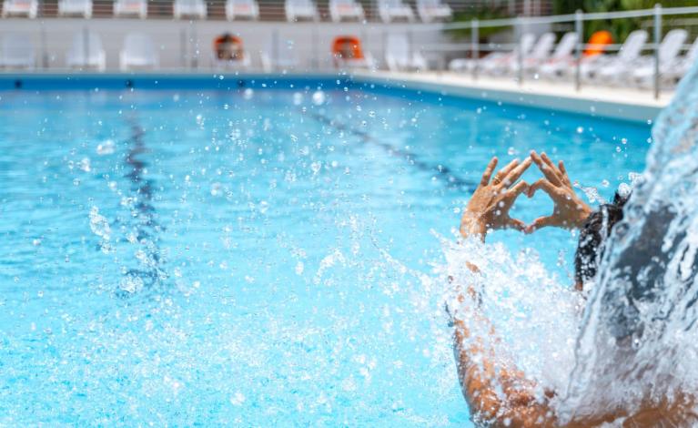Persona in piscina forma un cuore con le mani.
