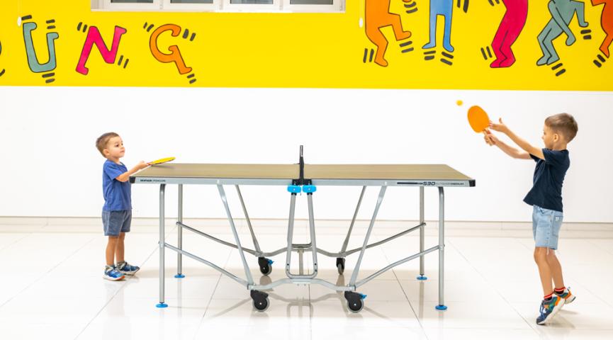 Kinder spielen Tischtennis in einem bunten Raum.
