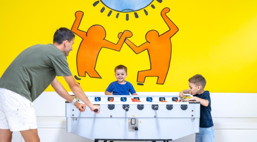 Sie spielen Tischfußball vor einem bunten Wandbild.