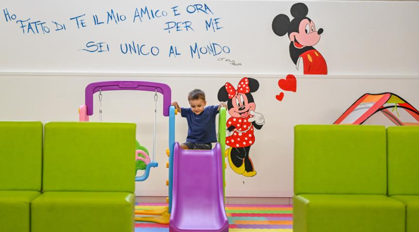 Kind spielt auf bunter Rutsche, Wand mit Disney-Figuren dekoriert.