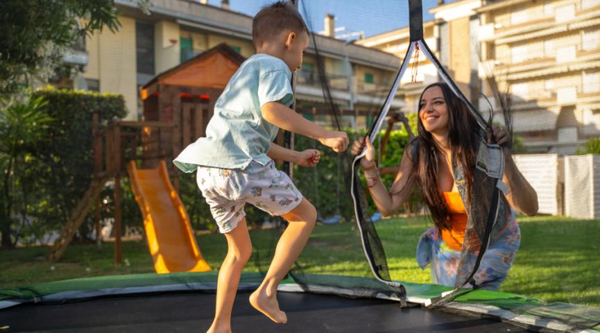 Kind und Frau spielen auf einem Trampolin im Garten.