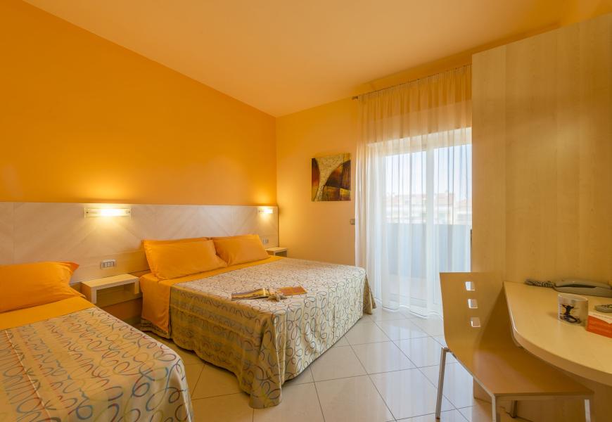 Camera con letto matrimoniale e singolo, pareti arancioni, luminosa finestra.